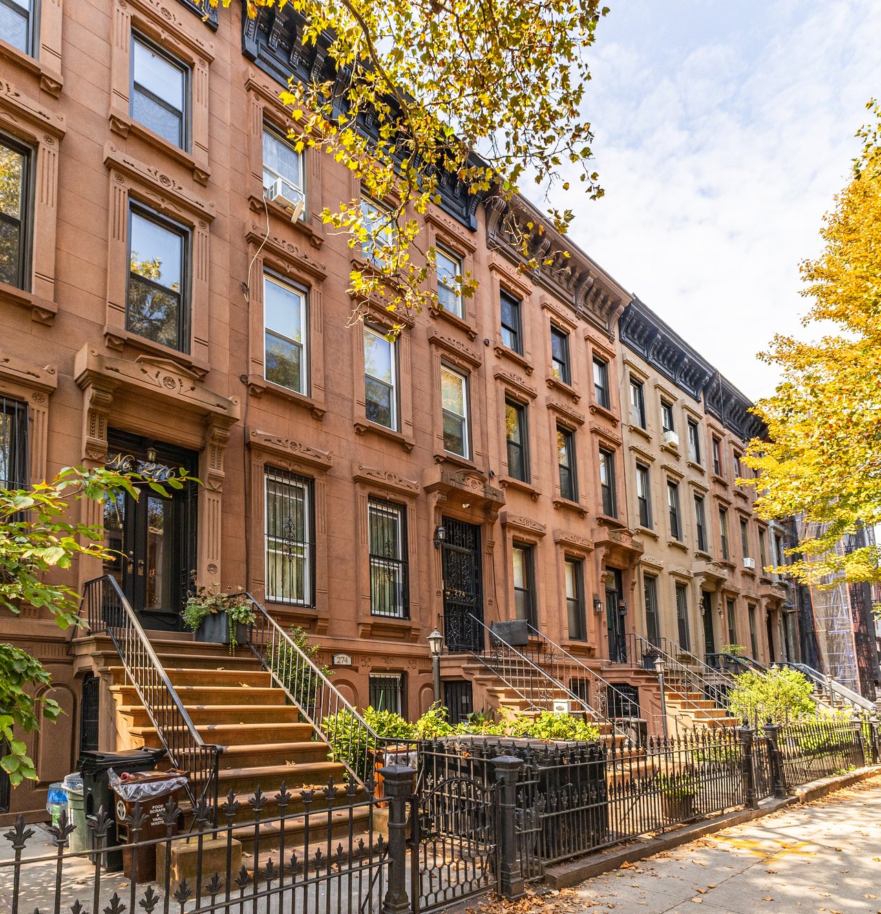 Broadway in Williamsburg, Brooklyn, featuring historic commercial architecture, the Williamsburgh Savings Bank, traditional brick buildings, mixed-use properties, and elevated subway infrastructure. The Parviz Team at Compass specializes in selling Brooklyn townhouses, brownstones, two-family homes, three-family buildings, multifamily properties, and mixed-use real estate.
