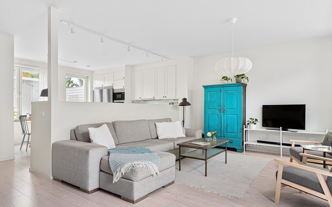 Open-plan living room with a gray sectional, turquoise cabinet, and white kitchen.