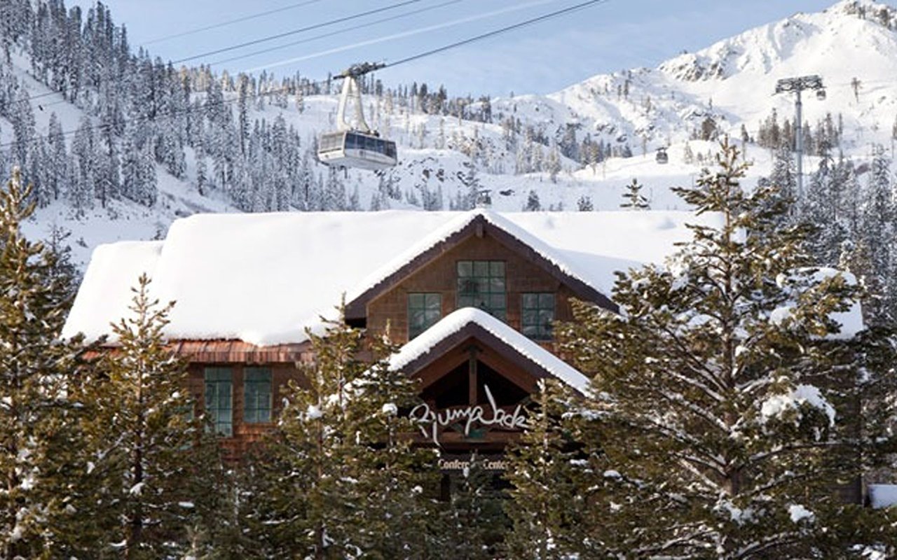 PlumpJack Squaw Valley Inn beneath a heavy blanket of snow, with a gondola and mountain slopes behind it.
