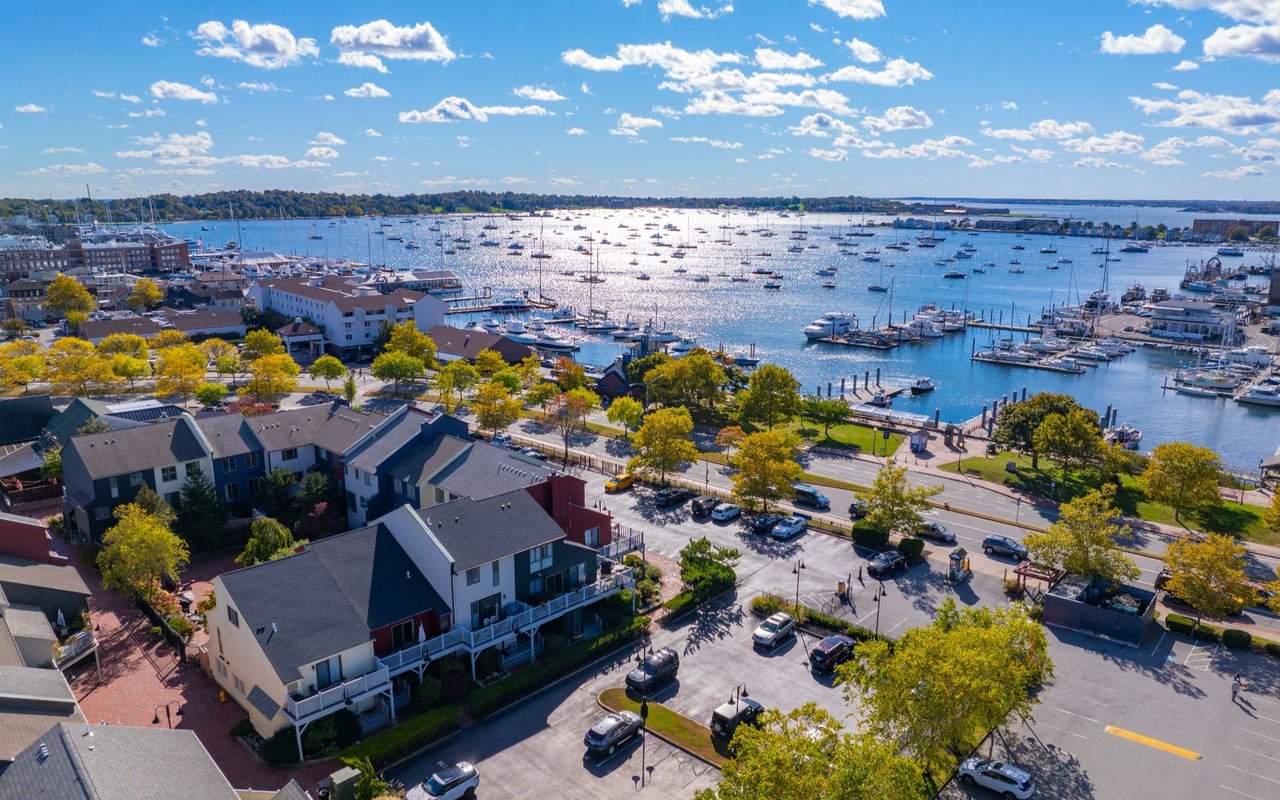 Aerial view of a harbor crowded with boats beside waterfront buildings and a parking area.