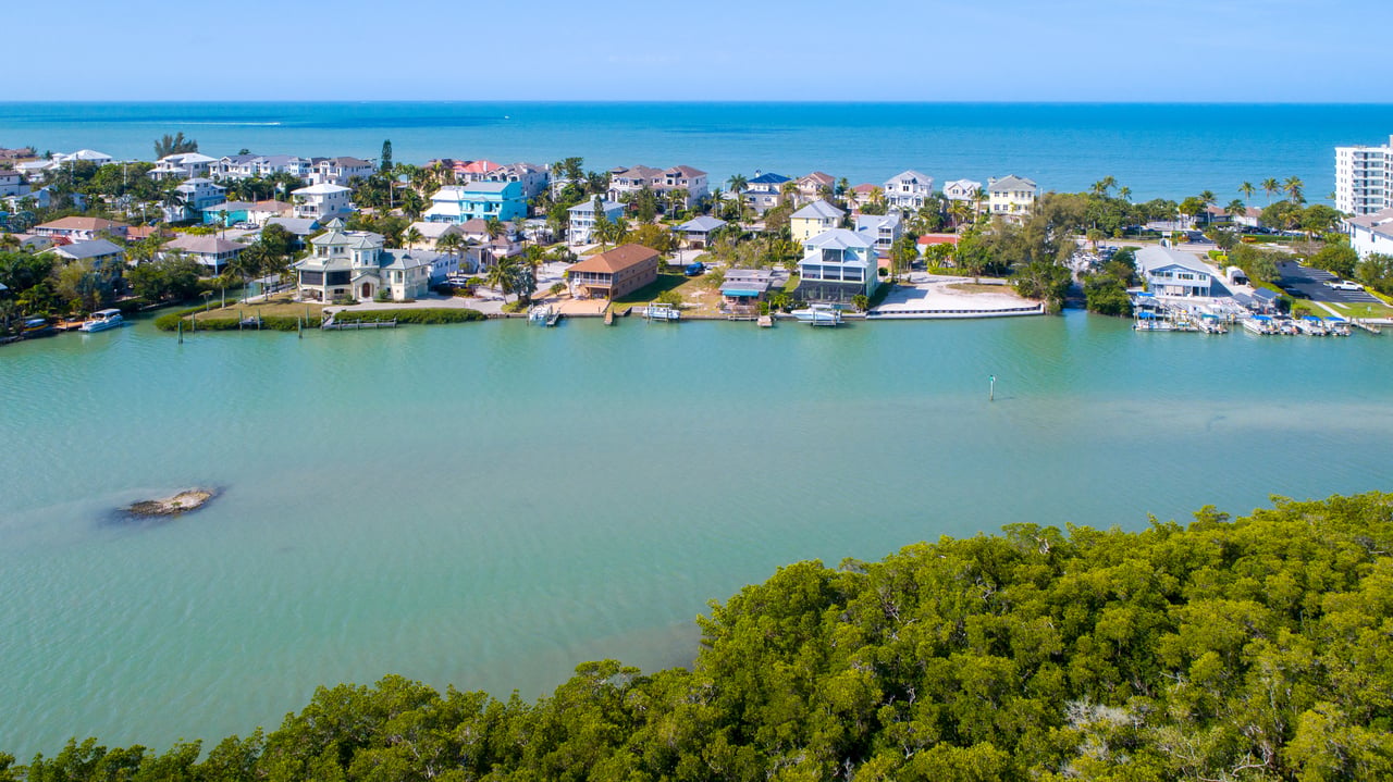 Aerial view of waterfront homes and docks along a Gulf-access waterway, with mangroves and the Gulf beyond.