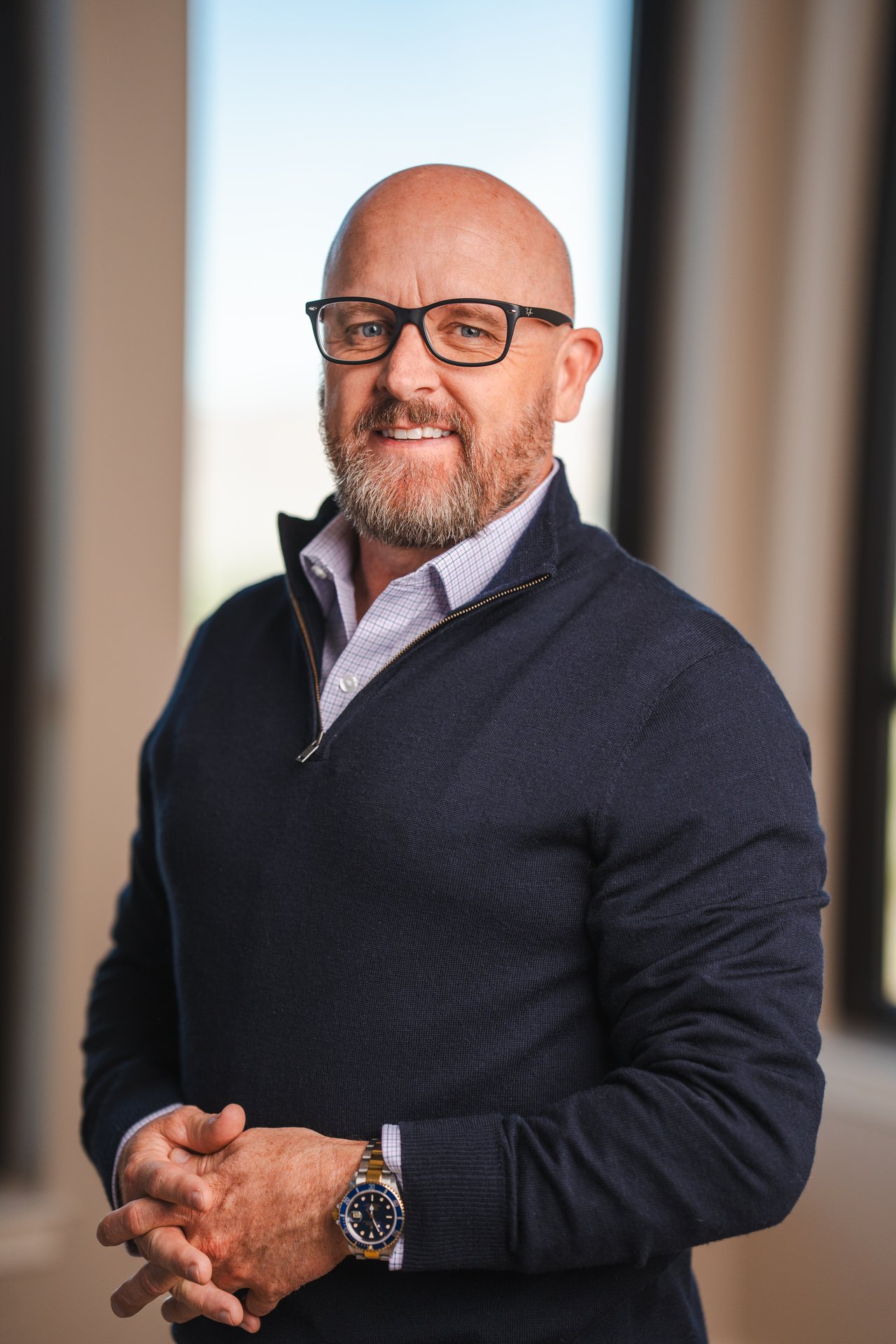 Scott Silva in glasses and a navy sweater, standing with his hands clasped.