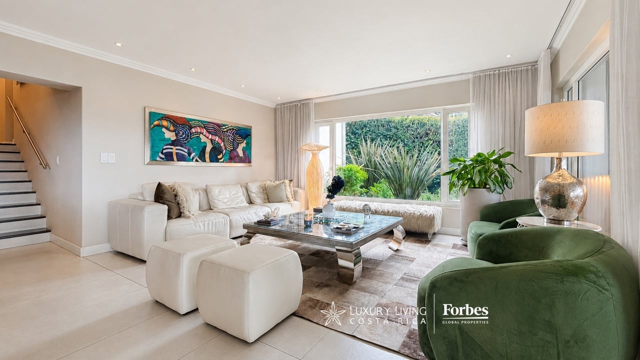 Living room with a white sectional, green armchairs, and large windows overlooking lush greenery.