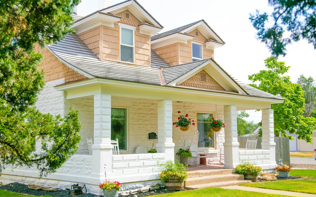 Two-story house with a covered white-columned porch and colorful flower planters.