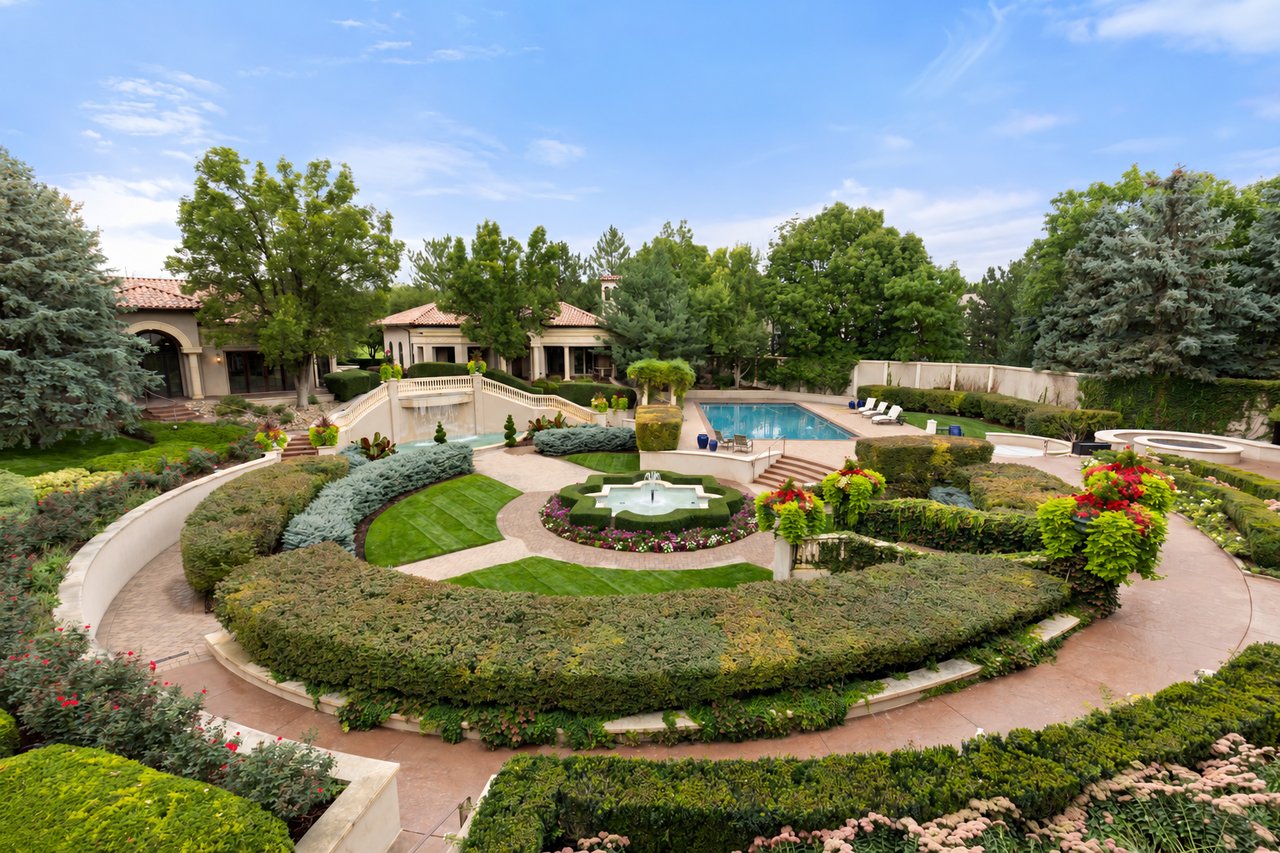Landscaped backyard with a pool, central fountain, curved paths, and the home beyond.