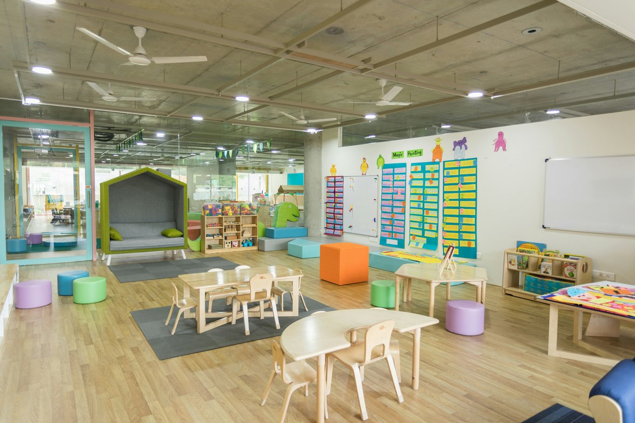 Childcare classroom with low tables, colorful cushions, a reading nook, and children’s activity displays.