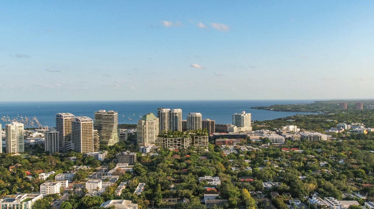 Aerial view of Coconut Grove high-rises, a marina, Biscayne Bay, and a planted-terrace development.