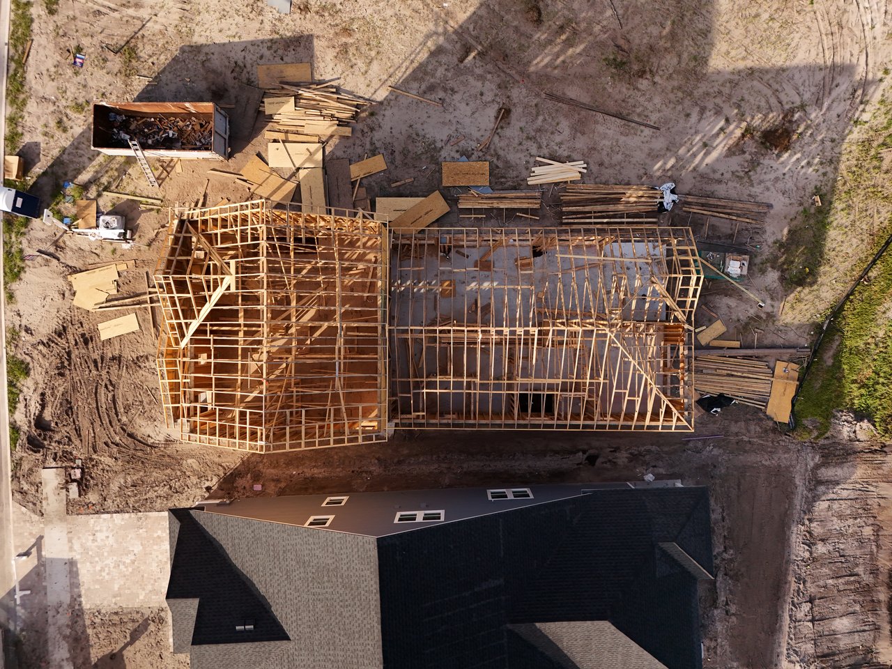 Aerial view of a home under construction, with exposed wooden framing and building materials across the lot.