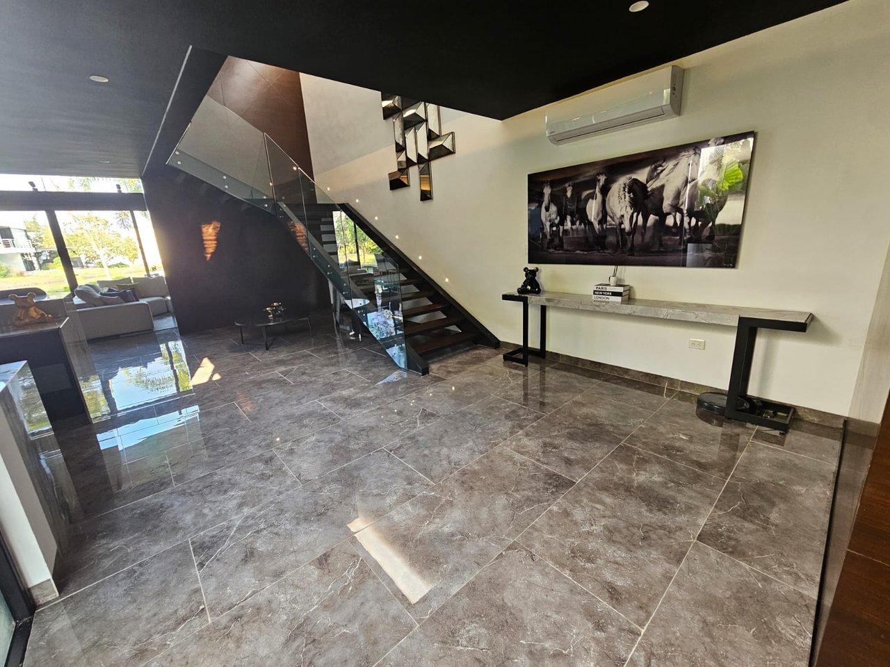 Modern tiled foyer with a glass-railed staircase and horse artwork above a console table.