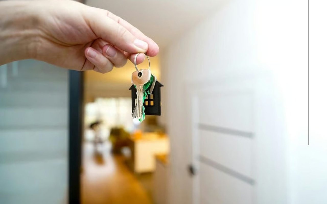 Hand holding house keys with a small house-shaped keychain by an open doorway.