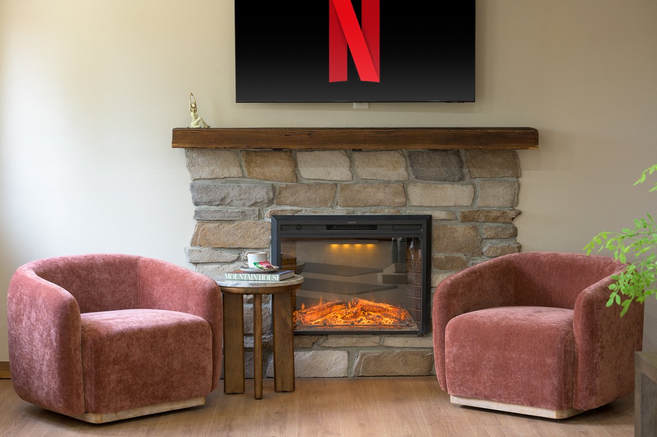 Living room with a stone fireplace, wood mantel, and two dusty-rose armchairs.