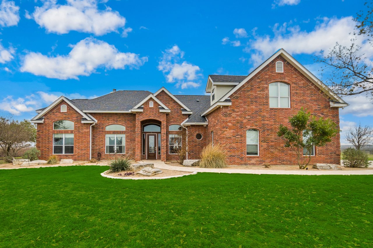 Red-brick house with multiple gables, an arched entry, and a broad green lawn.
