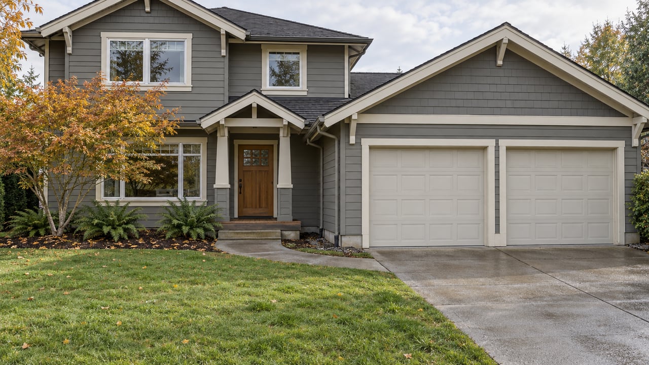 Updated gray gabled home with a deep green front lawn, double garage and copper-leaved maple beside the entry.