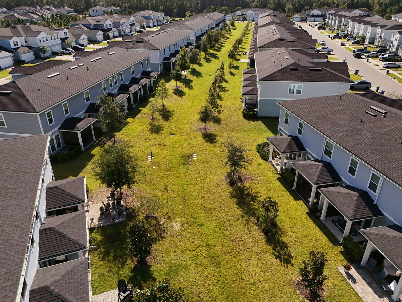 Aerial view of gray townhomes surrounding a long grassy common area with scattered trees.