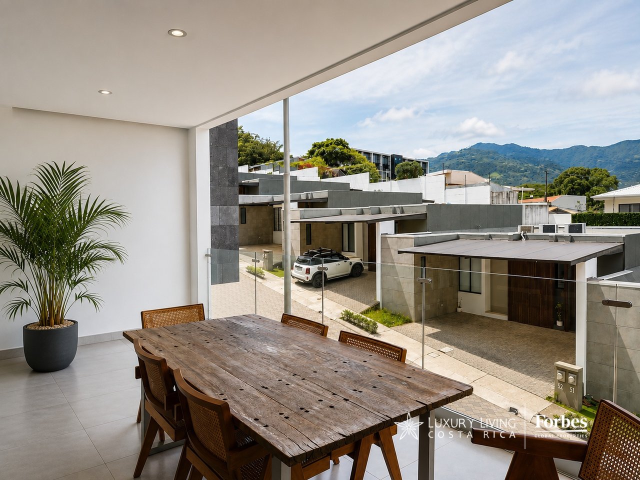 Covered dining terrace with a long wooden table, glass railing, and mountain views.