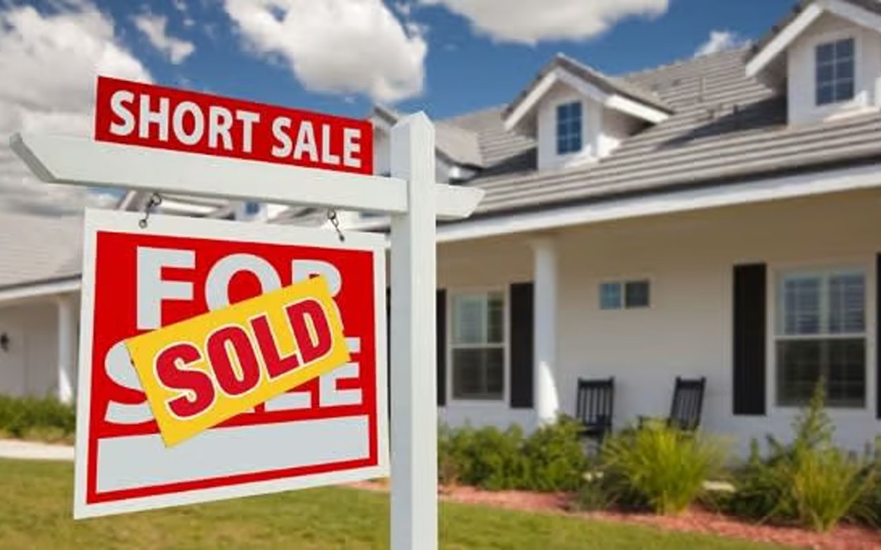 House with a “Short Sale” sign above a “For Sale” sign marked “Sold.”