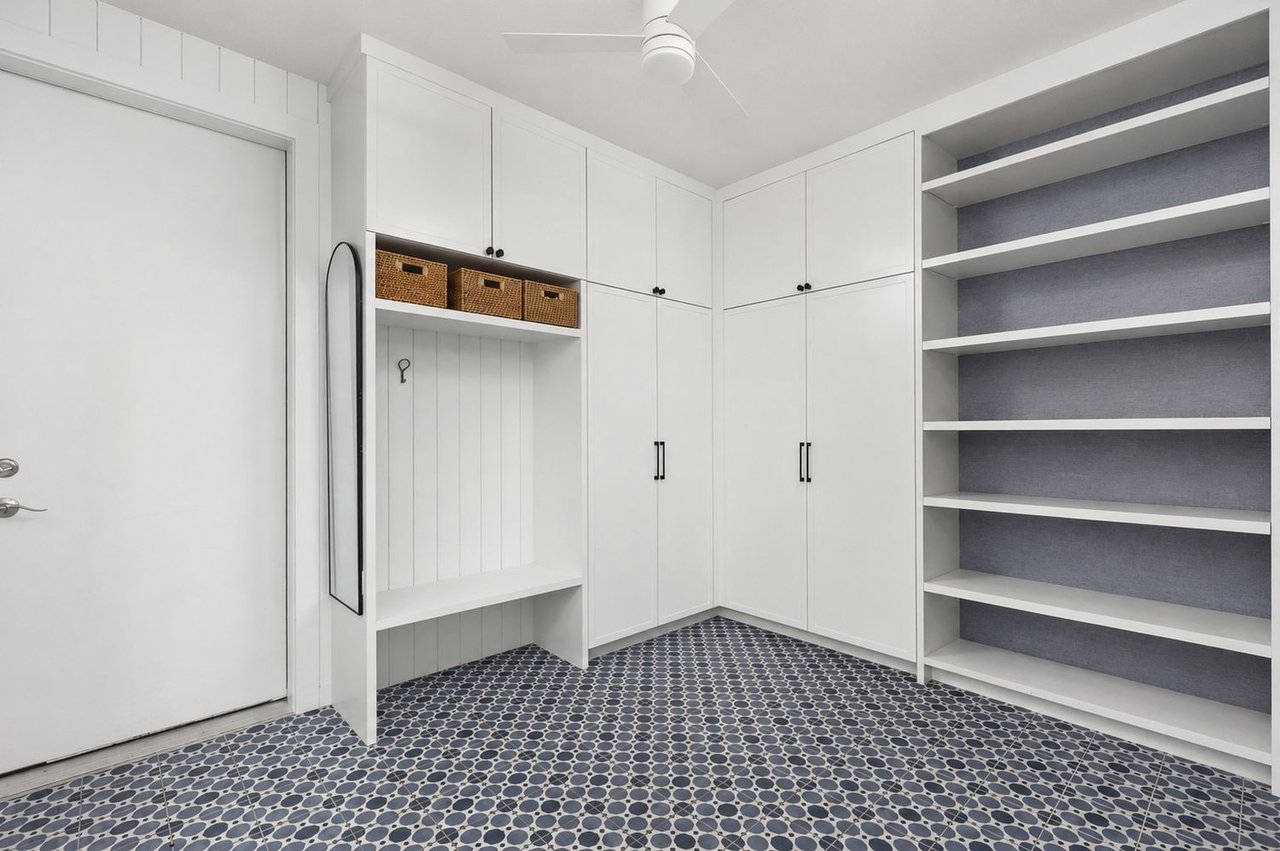 Mudroom with white built-in cabinets, a bench, open shelving, and patterned tile flooring.