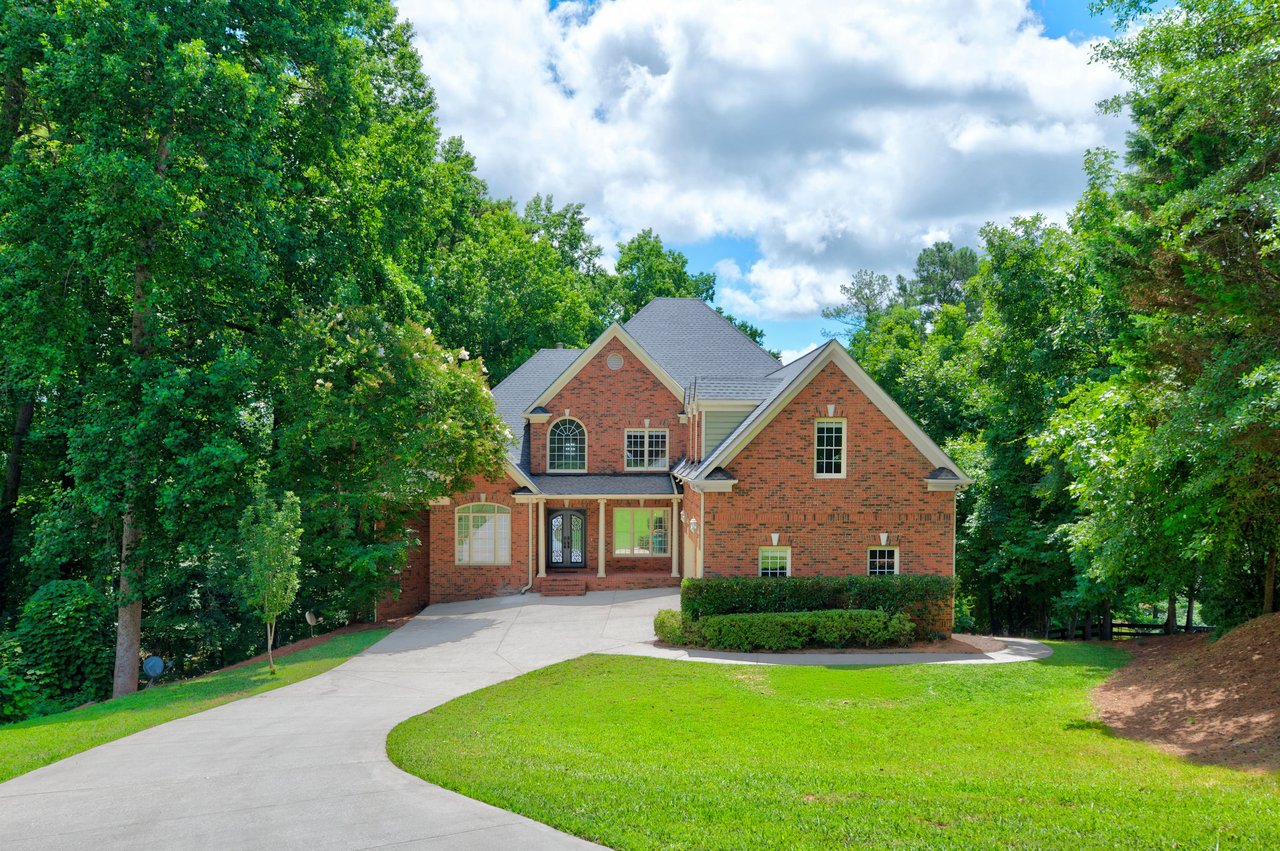 Red brick house framed by mature trees, with a curved driveway and broad front lawn.