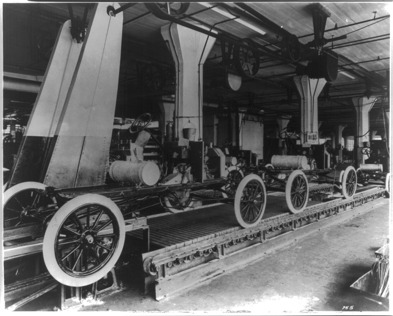 Early automobiles move along an assembly line inside the Highland Park Ford Plant.