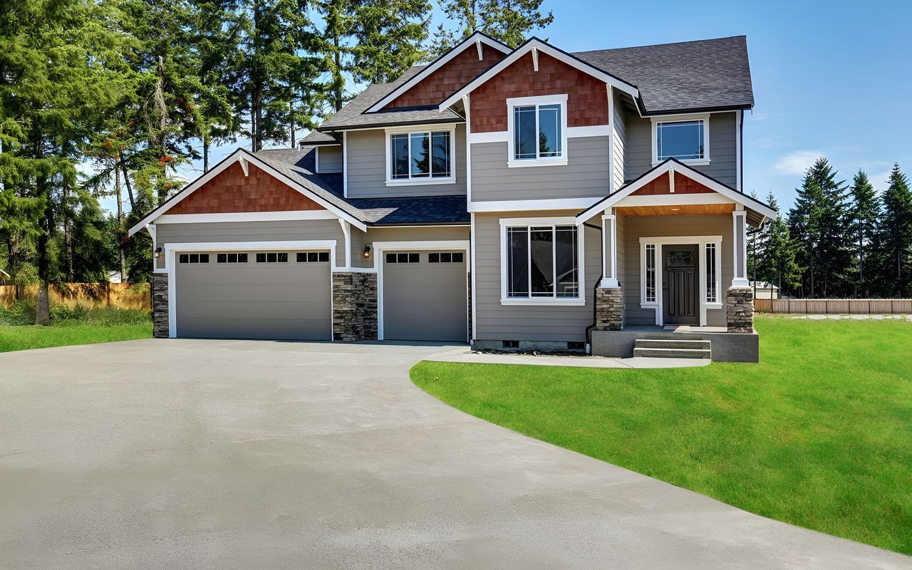 Two-story gray house with red-brown gables, three garage bays, and a broad driveway.