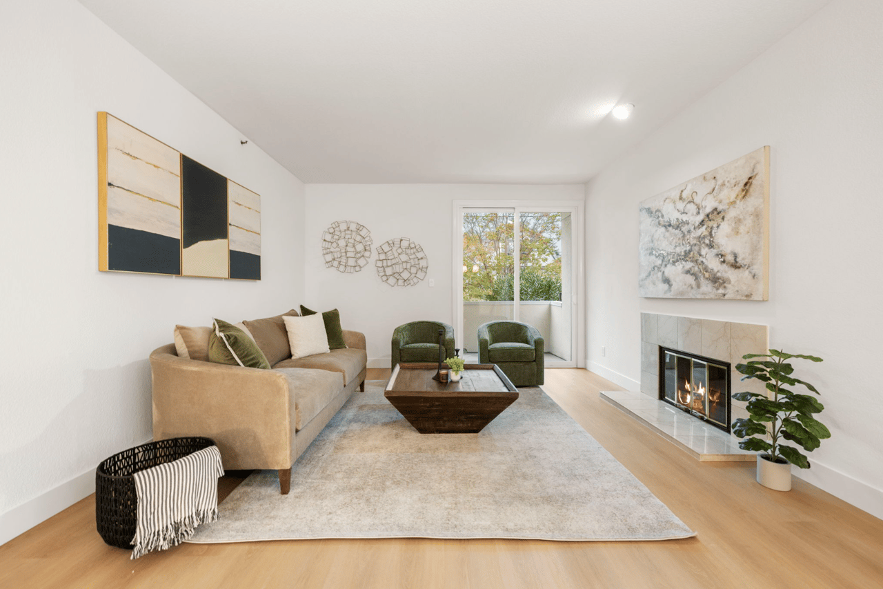 Staged living room with a beige sofa, green chairs, and a lit fireplace.