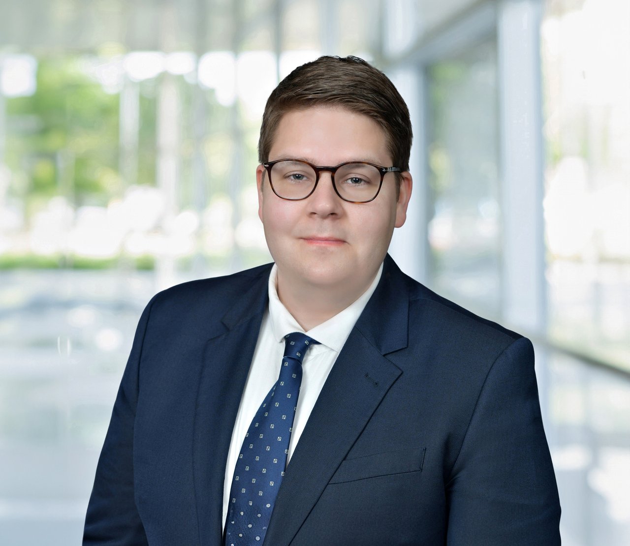 Gereon Wiese wearing glasses and a navy suit against a bright office-window backdrop.