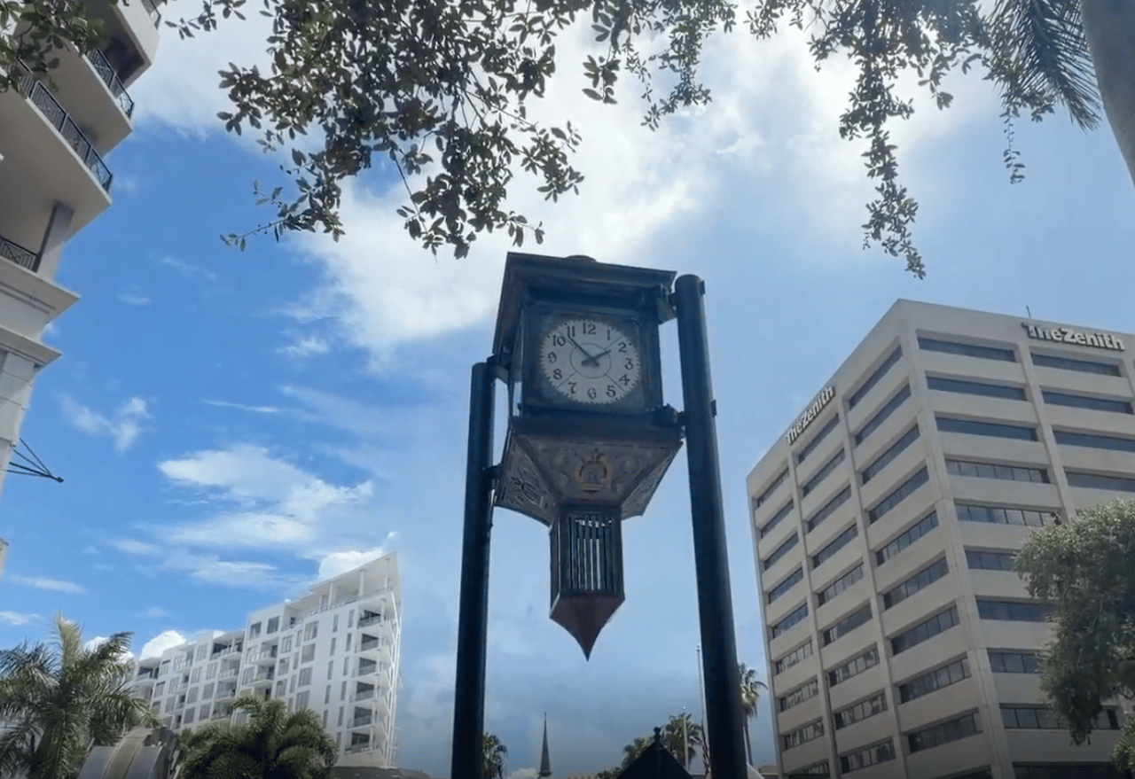 Downtown Sarasota street clock framed by office buildings and leafy branches.