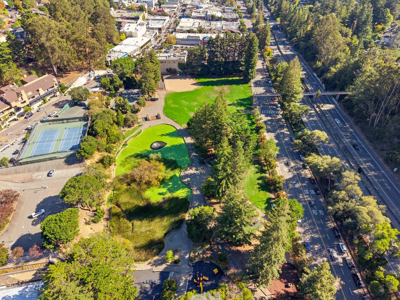 Aerial view of a landscaped park with tennis courts, lawns, and a tree-lined roadway.