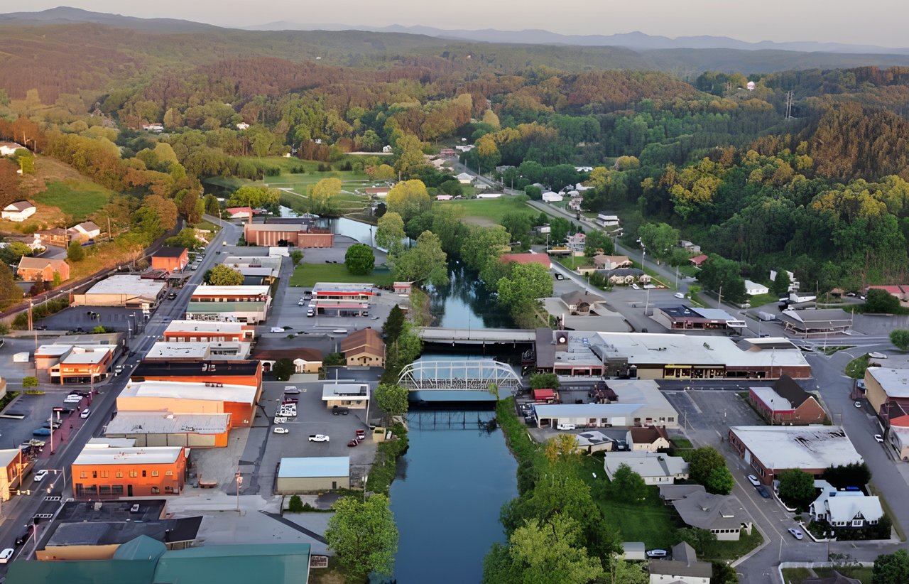 Aerial view of McCaysville, with a river running through downtown beneath wooded mountain ridges.