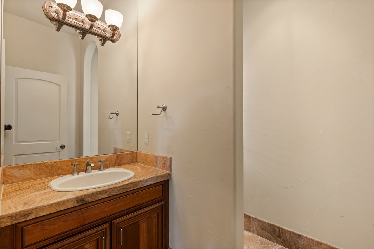 Bathroom vanity with a white oval sink, tan stone counter, large mirror, and textured partition.