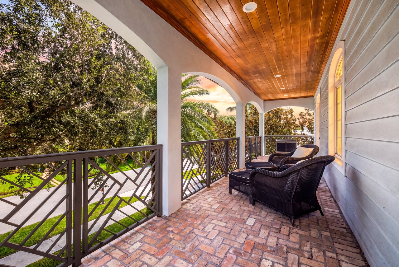 Covered brick-paver porch with a wood-plank ceiling, arched openings, and wicker seating overlooking the garden.