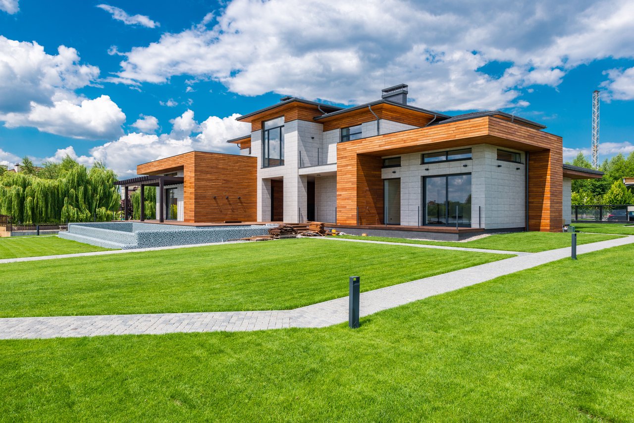 Modern two-story home with wood cladding, white stone walls, a broad lawn, and a long front water feature.