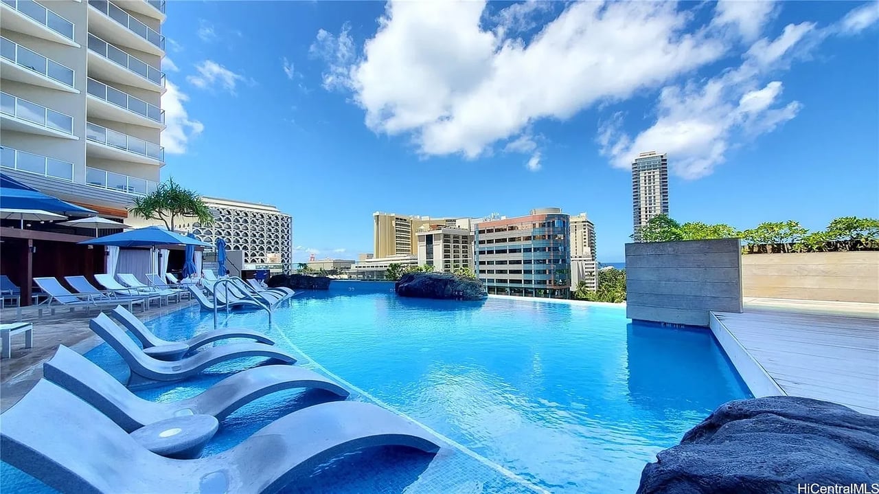Outdoor pool with in-water loungers overlooking Honolulu buildings and a glimpse of ocean.