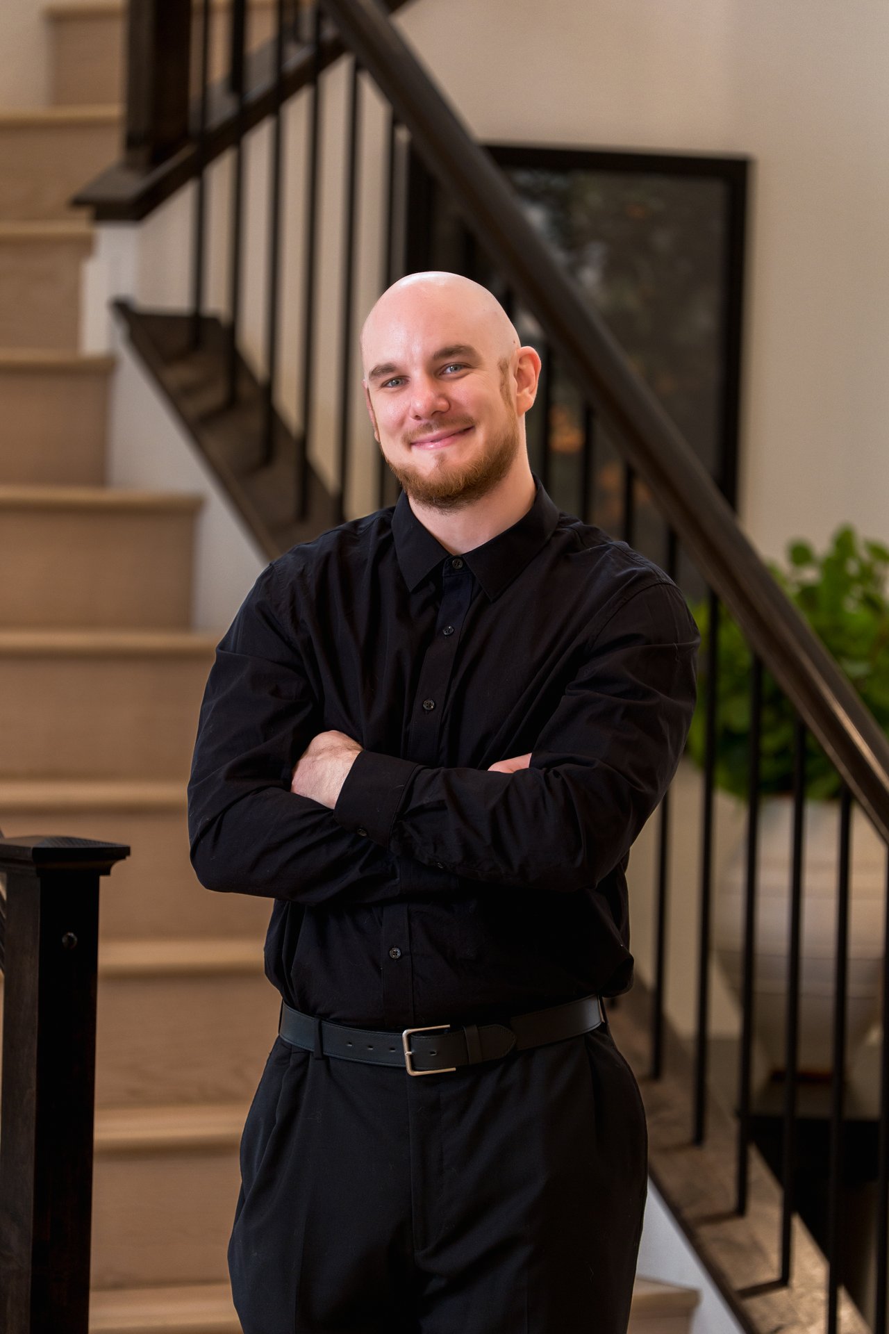 Cameron Potter in black, standing with arms crossed in front of a staircase.