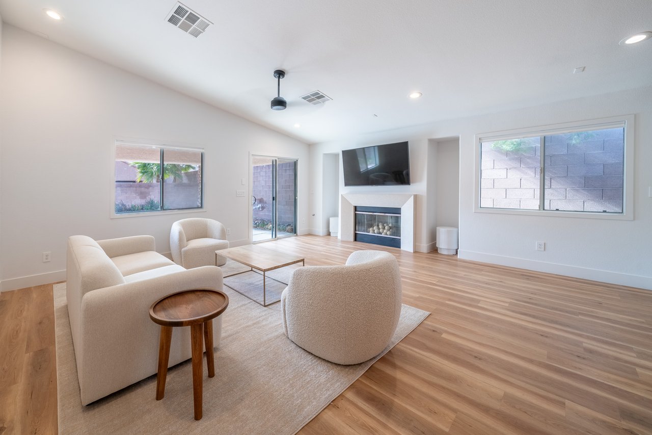 Furnished living room with cream seating, light wood floors, and a fireplace beneath a wall-mounted TV.