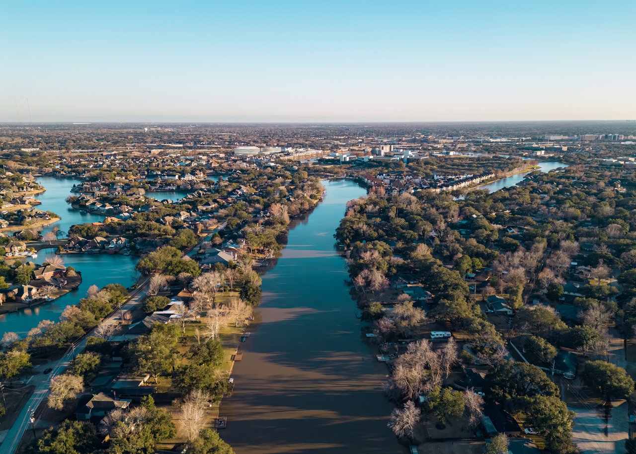 Sugar Land neighborhood beside a broad waterway, with tree-lined homes and distant urban development.