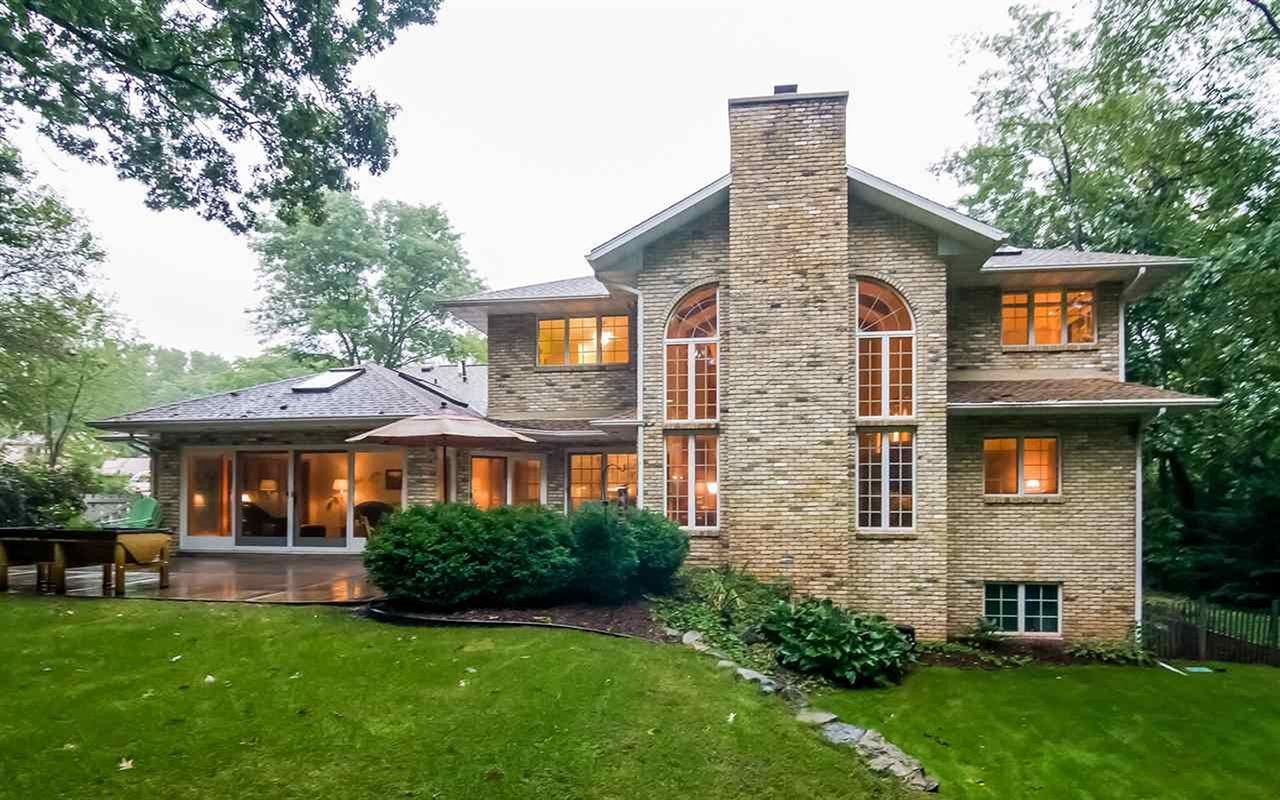 Brick home with arched windows, central chimney, and a covered patio overlooking a green lawn.