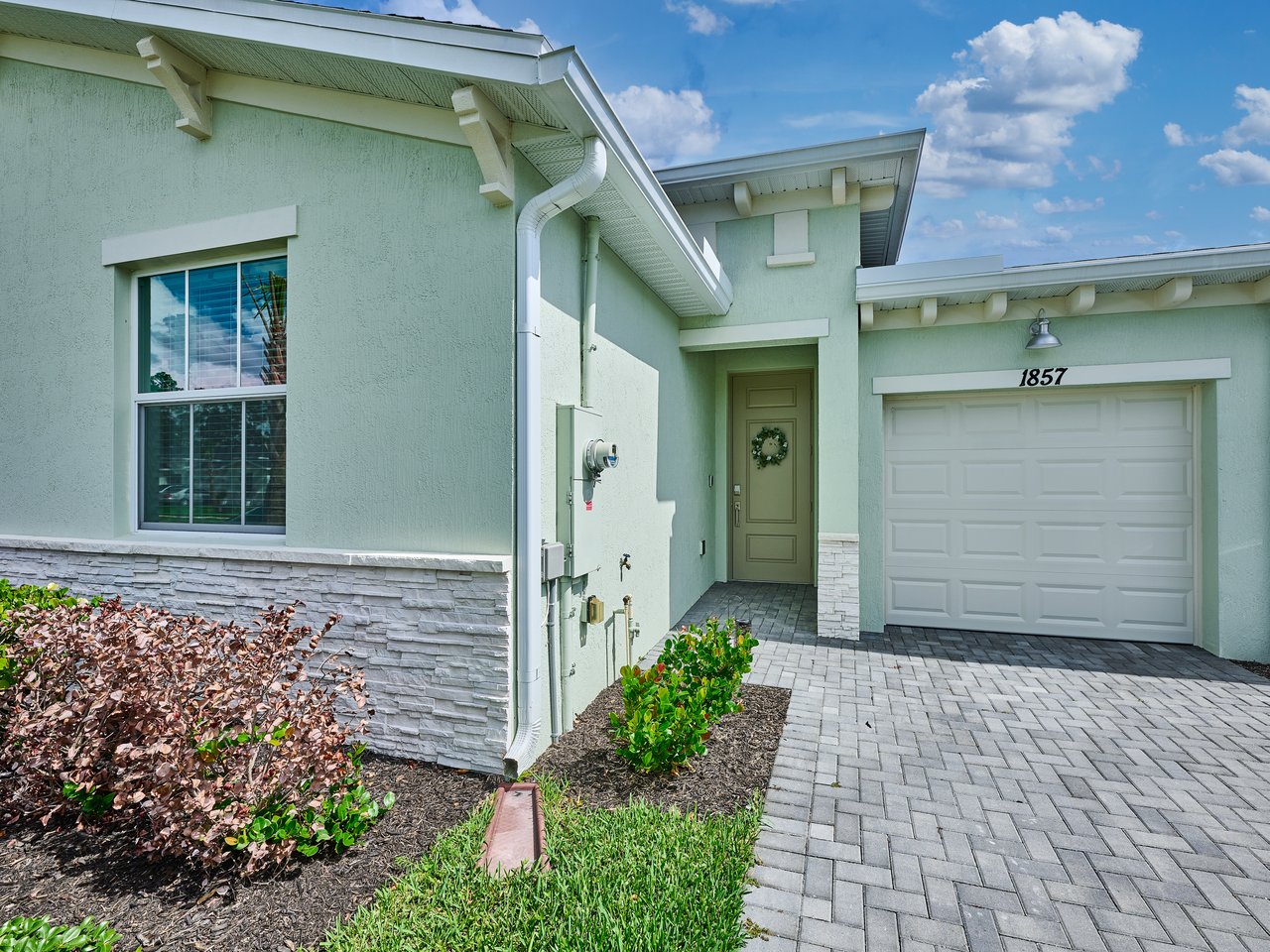 Pale green stucco home with a stone-trimmed facade, white garage door, and paver driveway.