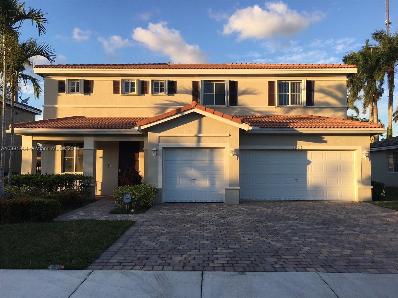 Two-story beige home with a red tile roof, twin garage doors, and a paved driveway.