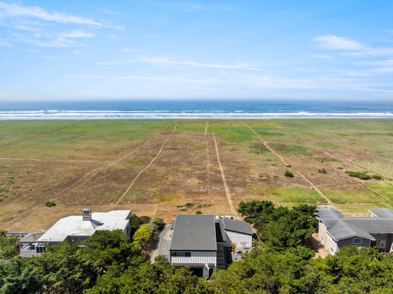 Aerial view of an oceanfront home on the Oregon Coast with direct beach access, expansive coastal grasslands, and panoramic Pacific Ocean views