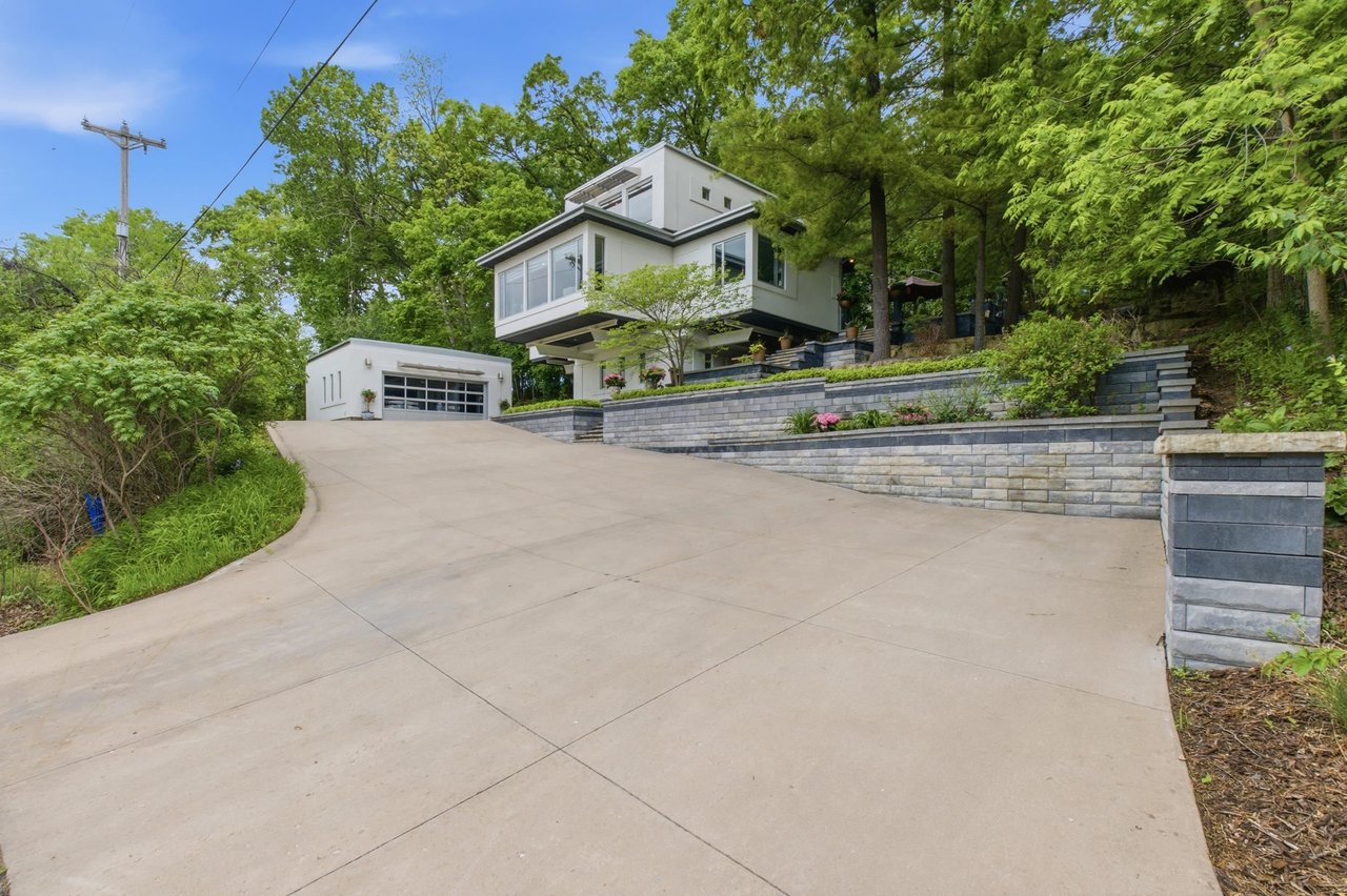 Contemporary home at 3702 Pheasant Branch Road in Middleton, WI, surrounded by mature trees with terraced landscaping and a sloped driveway.