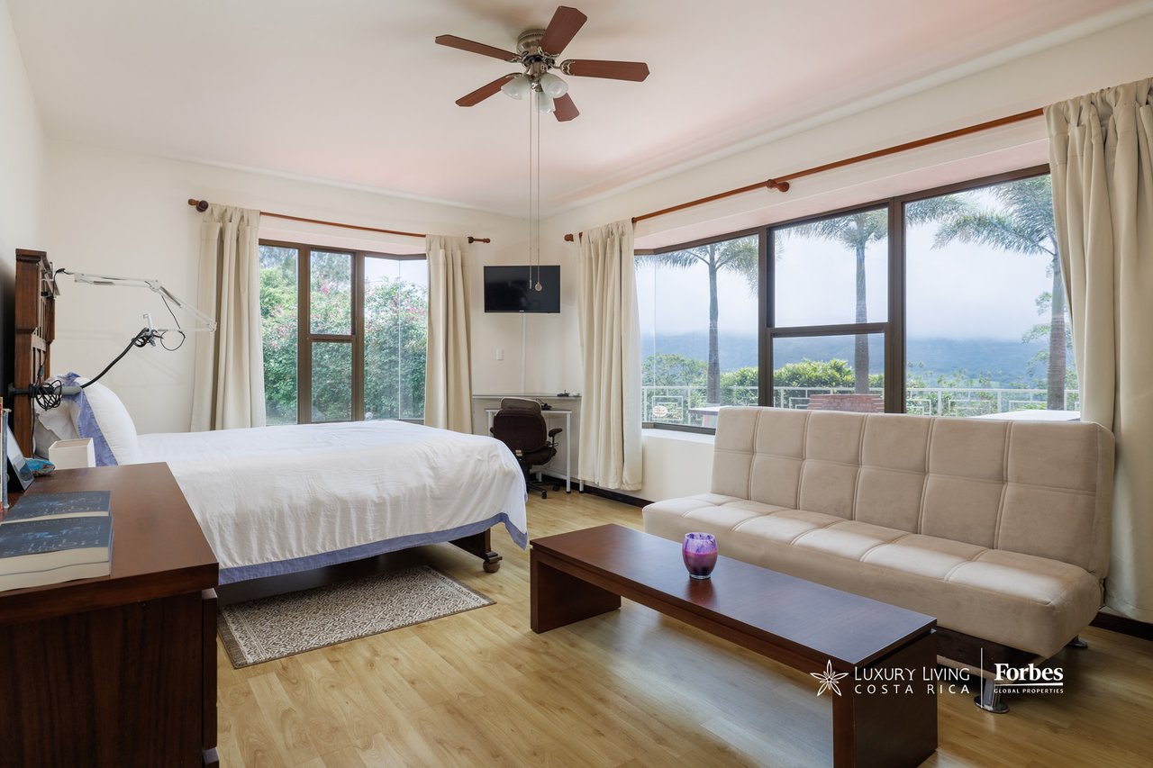 Bedroom with a white bed and sofa beside large windows overlooking misty mountains.