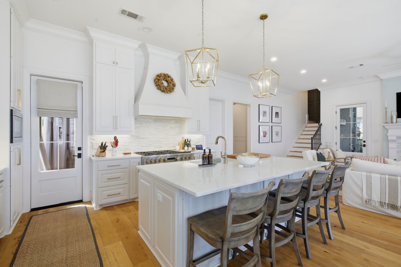 Bright white kitchen with a large marble island, gold pendant lights, and gray bar stools.