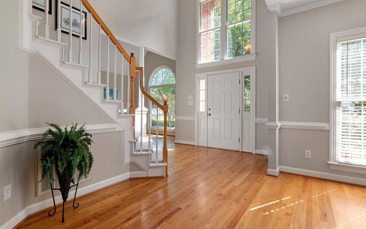 Two-story foyer with hardwood floors, a staircase, and tall windows beside the front door.
