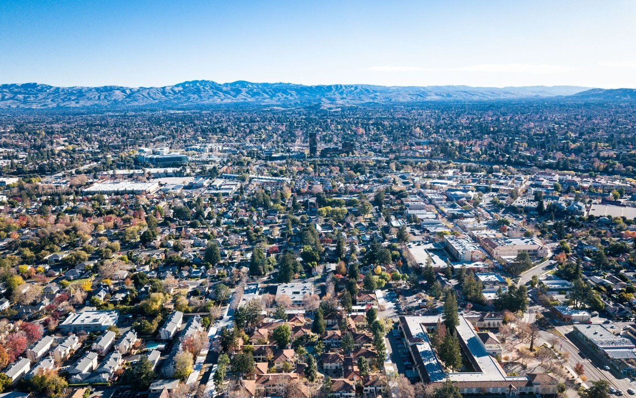 Aerial view of San Jose neighborhoods and commercial buildings, with hills on the horizon.