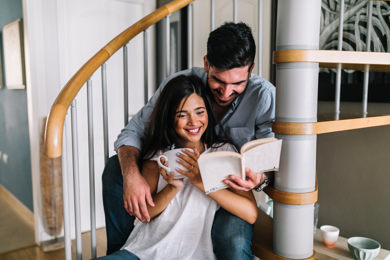 Couple sharing a book and mug while sitting together on a curved staircase