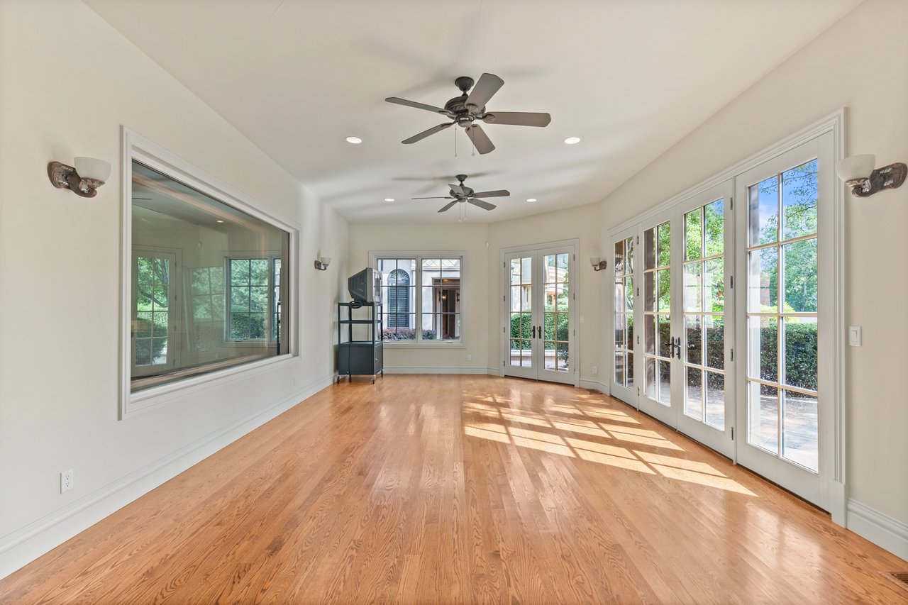 Sunroom with polished hardwood floors, two ceiling fans, and expansive windows and glass doors.