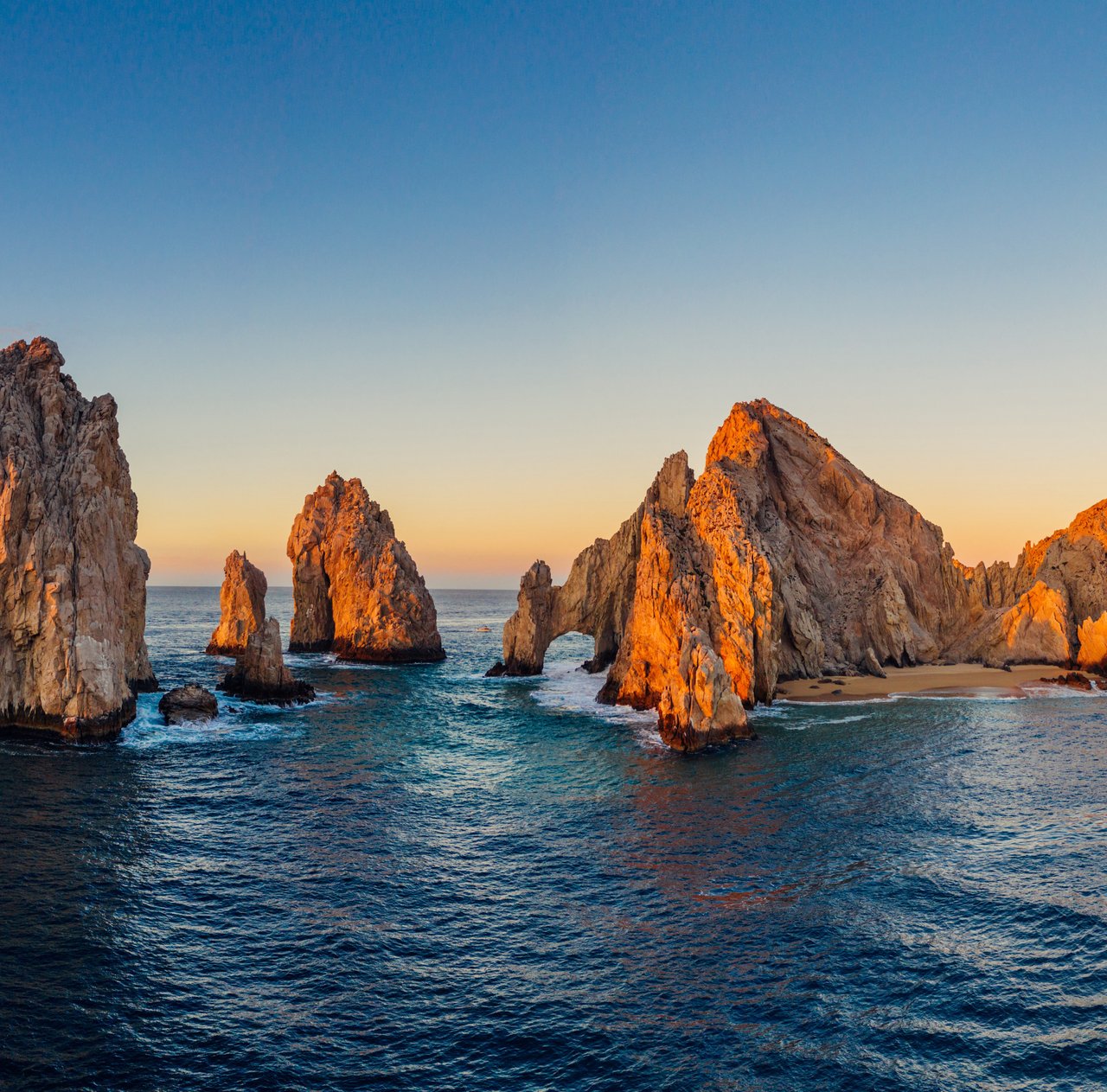 El Arco at Land’s End, with golden-lit rock formations rising from the ocean.