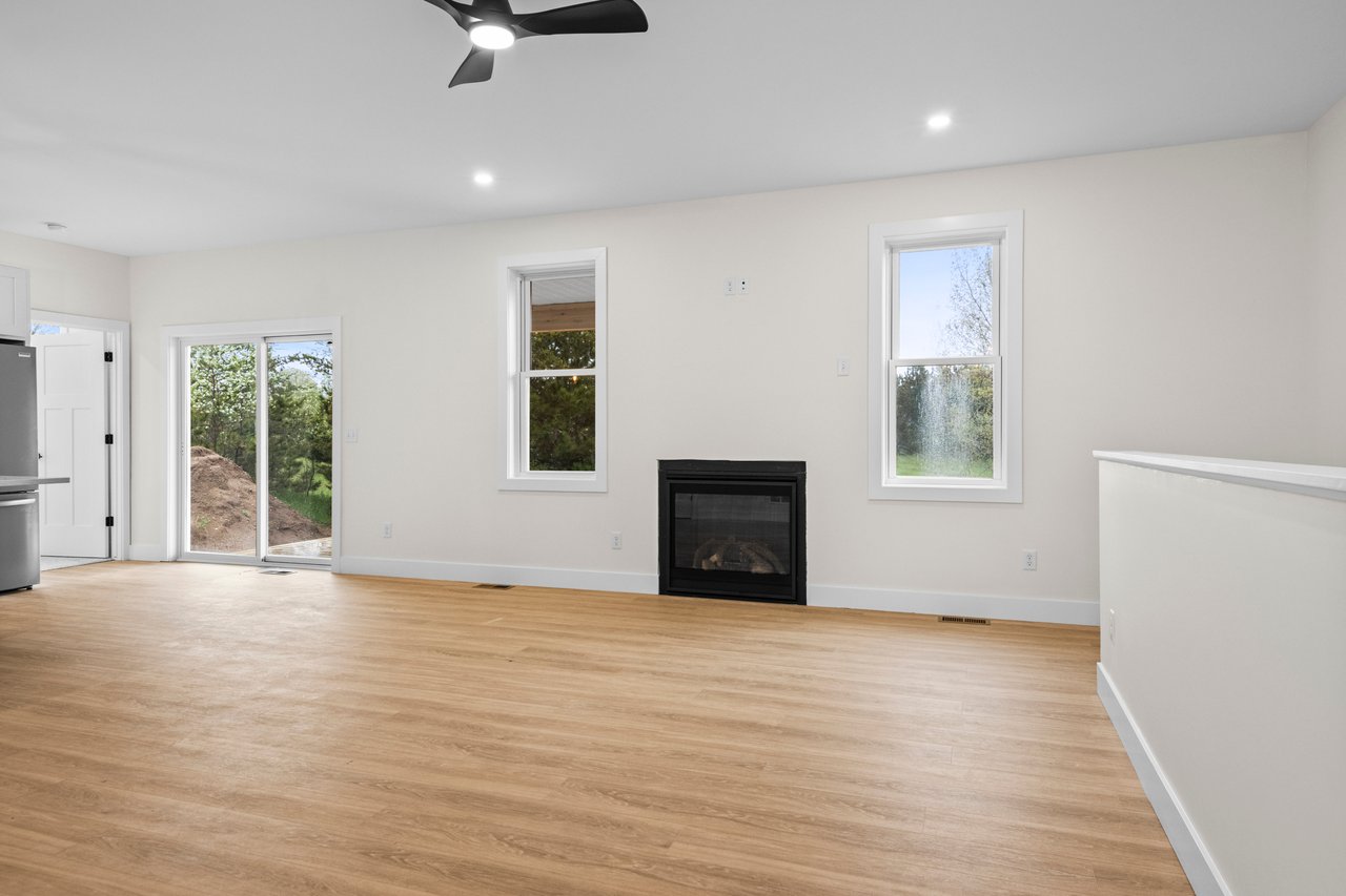 Vacant living room with a black fireplace, light wood floors, and sliding glass doors.