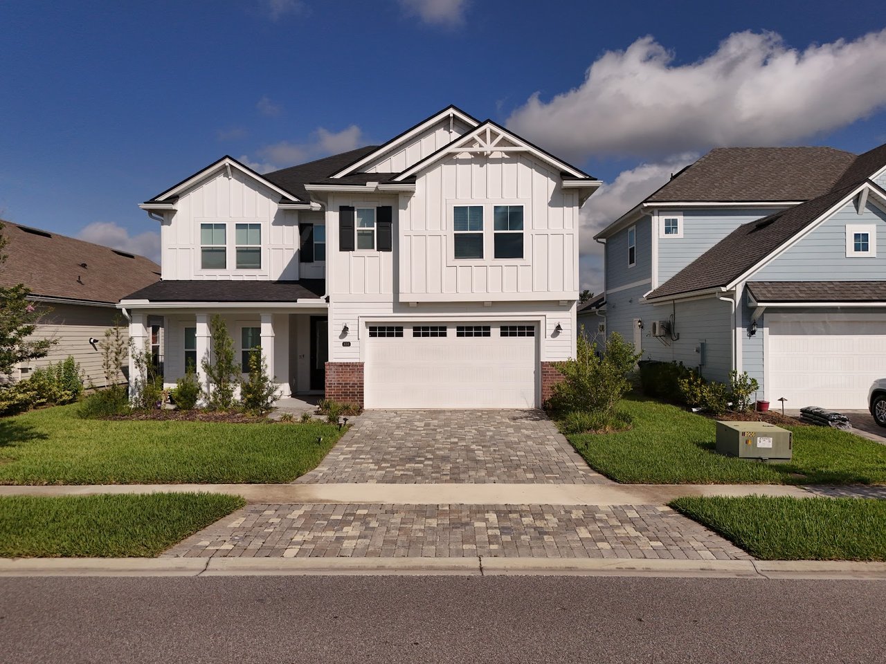 White two-story home with brick accents, a covered porch, and a paver driveway.